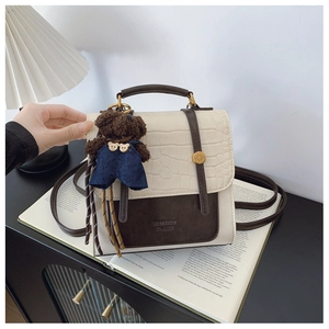 Close-up of minimalist crocodile-patterned bag with teddy bear charm on open magazine