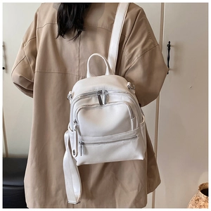 Detail of mini white PU leather backpack featuring silver zippers and wide woven straps