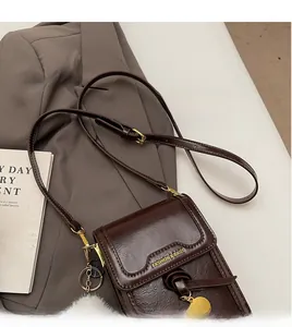 Detail view of smooth brown leather phone bag with gold chain and white fur ball charm