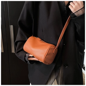 Détail du sac cylindre en cuir grainé orange avec logo Delvaux embossé sur le côté
