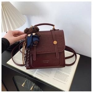 Detail of vintage burgundy leather handbag featuring crocodile texture and cute bear charm