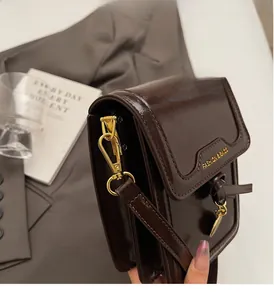Detailed shot of dark brown glossy leather shoulder bag with golden clasp and logo