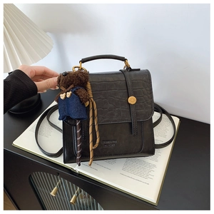Detail of black crocodile texture backpack with gold buckle and plush bear pendant