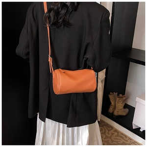 Détail d'un sac cylindrique orange porté avec un blazer noir et une jupe blanche