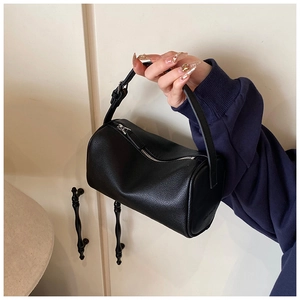 Détail d'un sac Boston en cuir grainé noir porté à la main dans un décor minimaliste