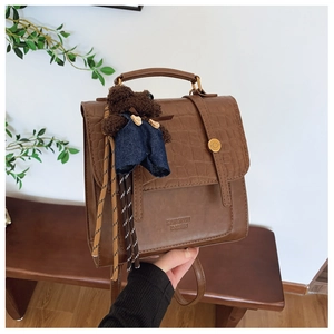 Detail of brown faux leather backpack with crocodile texture and cute bear charm