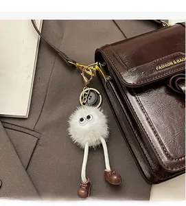 Detail of a cute white plush pendant with large eyes on a brown leather crossbody bag