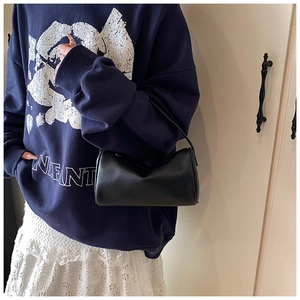 Détail du sac cylindrique noir en cuir grainé porté avec un sweat et une jupe en dentelle