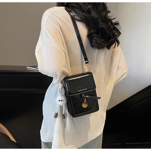 Detail of a black patent leather crossbody phone bag with a cute white plush monster charm