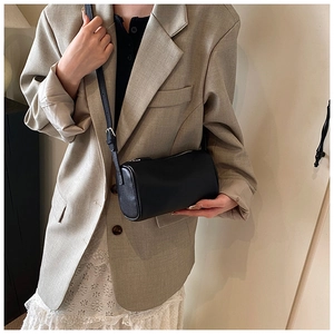 Détail du sac polochon en cuir noir texturé porté avec une veste de blazer beige élégante