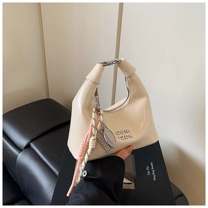Détail d'un sac à main beige brillant avec boucles argentées et pendentif raquette