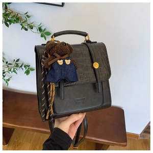 Detail of black backpack with crocodile texture flap and cute bear plush charm accessory