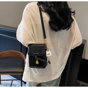 Detail of black glossy crossbody phone bag with long-legged doll charm and logo