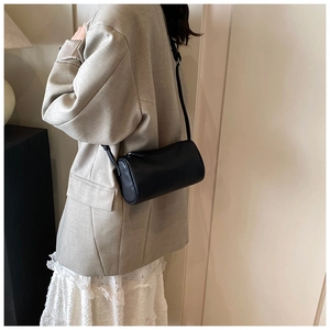 Sac cylindre noir minimaliste porté avec un blazer ajusté et une jupe en dentelle