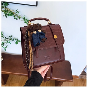 Detail of dark brown crocodile pattern faux leather backpack with plush bear charm
