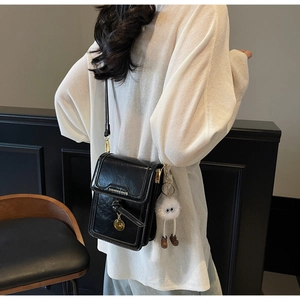 Detail of a black glossy leather crossbody bag with metal pendant and plush monster charm