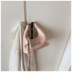 Détail du sac à bandoulière rose brillant avec logo métallique et pendentif raquette de tennis