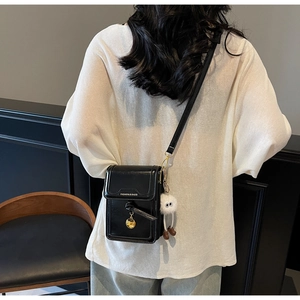Close-up of black crossbody phone bag with gold hardware and white plush charm on model