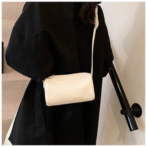Sac bandoulière cylindrique blanc en cuir texturé porté par un mannequin en intérieur