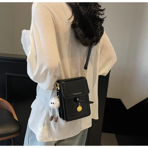 Detail of black glossy leather crossbody bag with a white plush monster charm and gold pendant