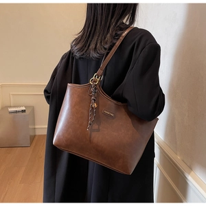 Detailaufnahme der braunen Tragetasche mit Metallplakette und dekorativem geflochtenem Quasten