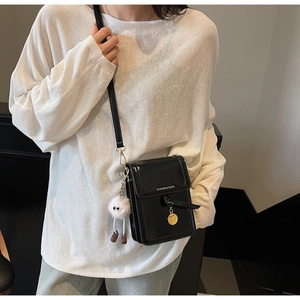 Detail of a black glossy crossbody bag with white monster plush charm and printed text