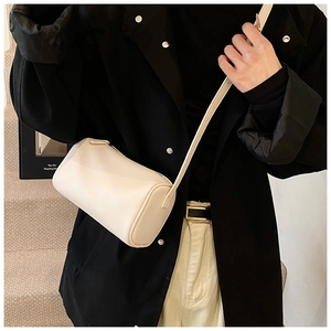 Vue détaillée du sac cylindrique en cuir grainé crème porté par un mannequin