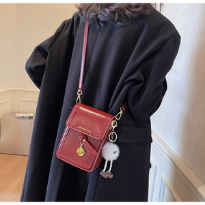 Detail of red patent leather crossbody bag with gold charms and a plush mascot pendant