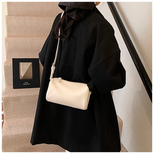 Gros plan du sac cylindrique crème en cuir grainé sur un manteau noir élégant