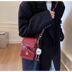 Detail of red crossbody bag with glossy finish featuring knot design and golden pendant