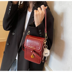 Close-up of wine red patent leather crossbody bag with plush charm and gold hardware