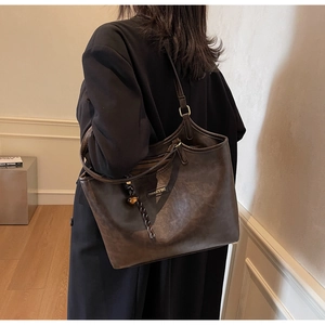 Detailansicht einer braunen Vintage-Tasche mit Metallplakette auf schwarzem Mantel