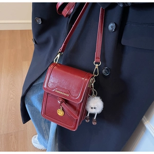 Detail of dark red crossbody phone bag with pompom charm on a black wool coat