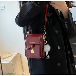 Macro shot of glossy burgundy leather crossbody bag with chic golden charm and plush ball