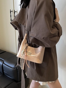 Sac à bandoulière demi-lune rose en cuir verni porté avec un trench-coat marron