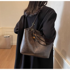 Detail einer großen dunkelbraunen Leder-Shopper-Tasche mit goldenem Glocken-Anhänger