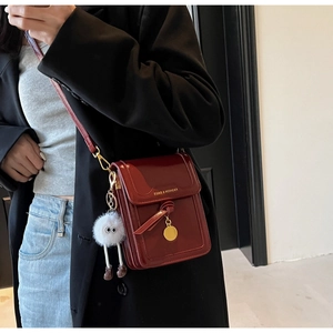 Detail of burgundy crossbody bag with gold charm and quirky white plush keychain