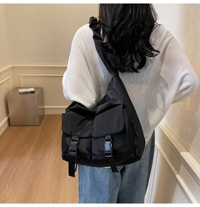 Detail of a black nylon messenger bag featuring double front buckle pockets and pleated strap