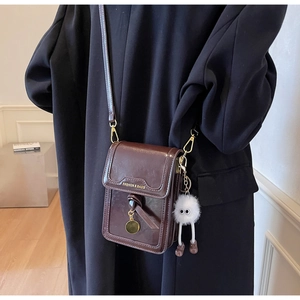 Close-up of dark brown vintage faux leather phone bag with gold lettering and plush charm