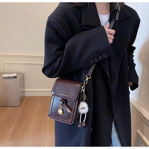 Detail of dark brown vintage crossbody bag with gold pendant and plush charm on a model