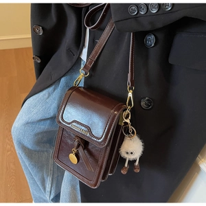 Detailed view of dark brown leather crossbody bag with fluffy monster charm and metal tag