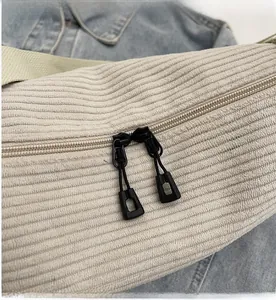 Detail der cremefarbenen Cord-Umhängetasche mit sanften schwarzen Doppel-Reißverschlüssen