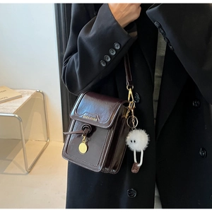 Detail of dark brown leather crossbody phone bag with gold charm and white plush monster charm