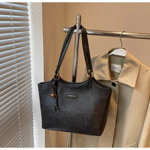 Detail der schwarzen matten Shopper-Tasche mit Goldlogo und Anhänger an Kleiderständer