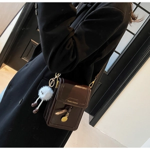 Detail of dark brown faux leather crossbody bag with fuzzy monster charm and gold hardware