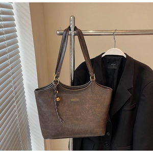 Detail der dunkelbraunen Leder-Shopper mit Metallemblem und dekorativem Webanhänger