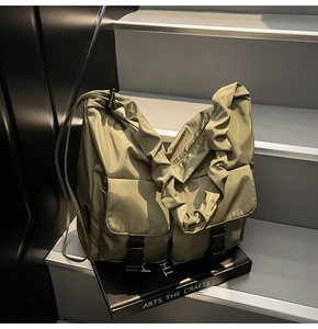 Close-up of olive green nylon bag with utility pockets and pleated shoulder strap detail
