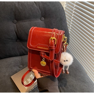 Detail view of burgundy leather crossbody bag with fuzzy monster charm on a sofa