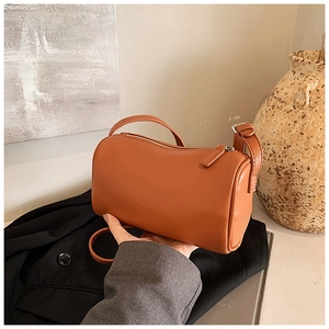 Détail d'un sac cylindre marron à motif lychee sur un costume noir haut de gamme