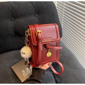 Detail of red textured crossbody phone bag with gold clasp and plush monster charm